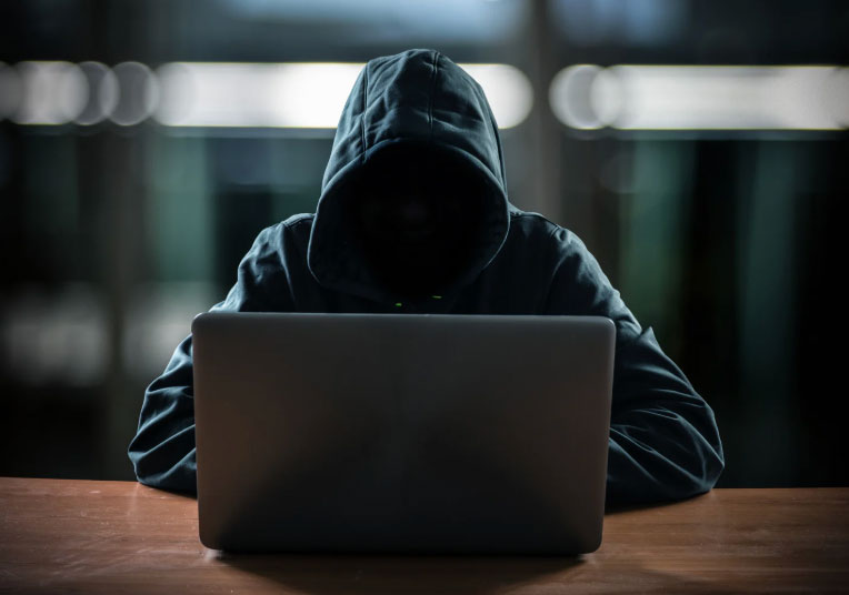 Hacker in a hoodie behind an open laptop